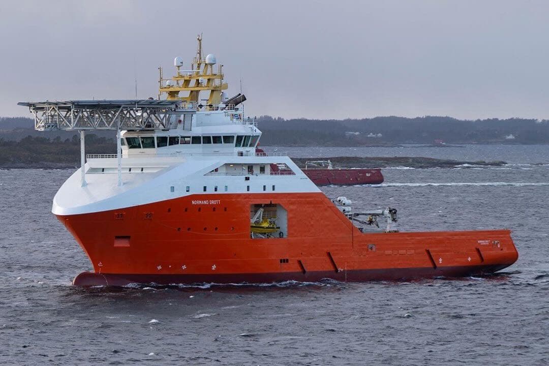 Oransje offshorefartøy med helikopterdekk på vei langs kysten